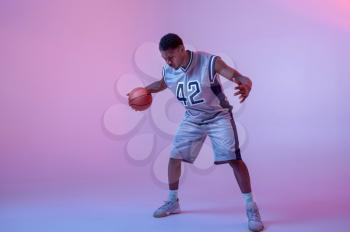 Basketball player practicing with ball in studio, neon background. Professional male baller in sportswear playing sport game, tall sportsman