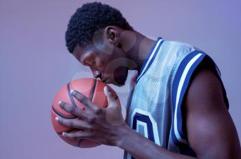 Serious basketball player poses with ball in studio, neon background. Professional male baller in sportswear playing sport game, tall sportsman