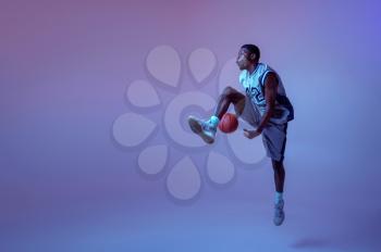 Basketball player practicing with ball in studio, neon background. Professional male baller in sportswear playing sport game, sportsman