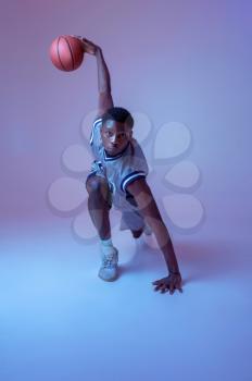 Muscular basketball player with ball shows his skill in studio, neon background. Professional male baller in sportswear playing sport game, tall sportsman