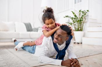 Smiling father and little daughter poses in living room. Dad and female child leisures in their house together, happy relationship
