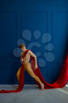 Male ballet dancer performing with red cloth in dancing studio, blue walls on background. Performer with muscular body, grace of movements
