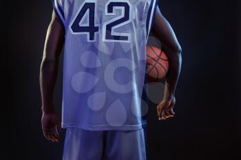 Basketball player poses with ball in studio, back view, black background. Professional male baller in sportswear playing sport game, tall sportsman