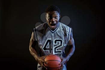 Aggressive basketball player poses with ball in studio, black background. Professional male baller in sportswear playing sport game, tall sportsman