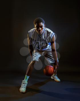 Basketball player with ball, practicing in action in studio, black background. Professional male baller in sportswear playing sport game, tall sportsman