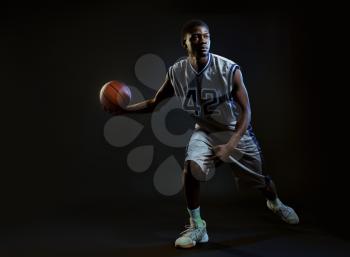Muscular basketball player with ball shows his skill in studio, black background. Professional male baller in sportswear playing sport game, tall sportsman