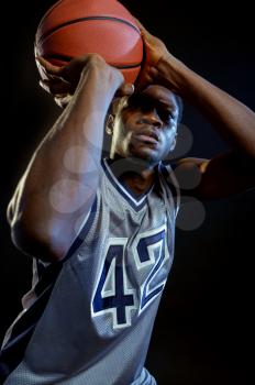 Basketball player throws a ball in studio, black background. Professional male baller in sportswear playing sport game, tall sportsman