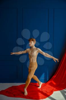 Male ballet dancer, performing in action, dancing studio, blue wall and red cloth on background. Performer with muscular body, grace and elegance of dance