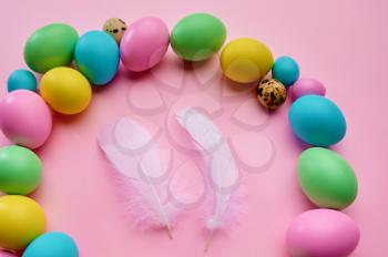 Colorful easter eggs and two white bird feathers on pink background, top view. Paschal food, event decoration, spring holiday celebration symbol
