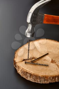 Hammer driving a nail into a stump, grey background, nobody. Professional instrument, builder equipment, fasteners, fastening and screwing tools