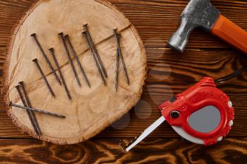 Screw nails, hammer and measuring tape on wooden background, top view, nobody. Professional instrument, carpenter equipment, fasteners, fastening and screwing tools