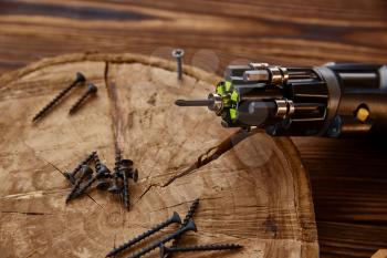 Screwdriver and self-tapping screws on stump, closeup, wooden background, nobody. Professional instrument, carpenter equipment, woodworker tools