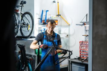 Bicycle repair in workshop, man fixing crank. Mechanic in uniform fix problems with cycle, professional bike repairing service