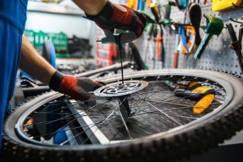 Bicycle assembly in workshop, man installs brake disk. Mechanic in uniform fix problems with cycle, professional bike repairing service