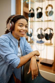 Young woman listening to music in headphones store. Female person in audio shop, showcase with earphones on background, buyer in the multimedia salon
