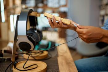 Woman connects headphones to phone in audio store, music fan. Female person in music shop, showcase with earphones on background, buyer in multimedia salon