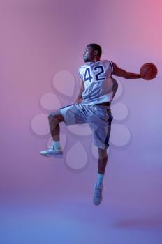 Basketball player jumping with ball in studio, neon background. Professional male baller in sportswear playing sport game