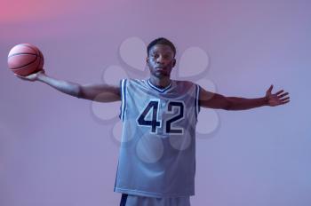 Athletic basketball player poses with ball in studio, neon background. Professional male baller in sportswear playing sport game, tall sportsman