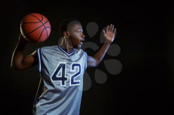 Aggressive basketball player poses with ball in studio, black background. Professional male baller in sportswear playing sport game, tall sportsman