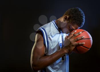 Focused basketball player poses with ball in studio, black background. Professional male baller in sportswear playing sport game, tall sportsman