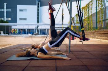Woman doing stretching exercise with ropes on sports ground outdoor. Slim female person in sportswear, outside fitness training, fit workout
