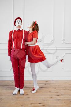 Two mime artists in red costumes, kissing scene. Pantomime theater, parody comedian, positive emotion, humour performance, funny face mimic and grimace