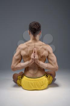 Yoga sits in classical pose with hands behind his back, meditation position, perfect stretching, grey background. Strong man doing yogi exercise, top concentration, healthy lifestyle