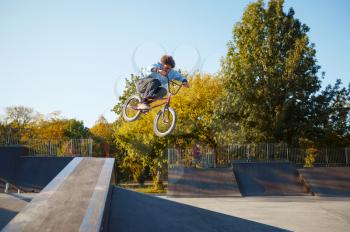 Young male bmx biker rides by railing in skatepark. Extreme bicycle sport, dangerous cycle trick, street riding, biking in summer park
