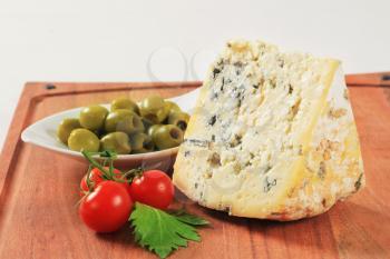 Wedge of blue cheese and bowl of olives on cutting board