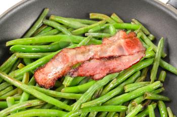 Green beans and bacon strips on a frying pan
