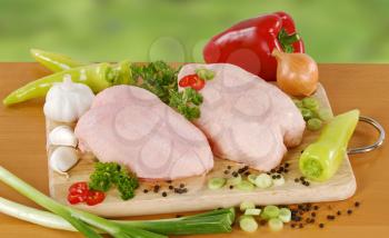 Raw chicken breasts and vegetables on a cutting board