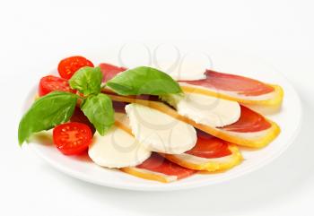 Sliced prosciutto crudo and mozzarella with fresh basil and tomatoes