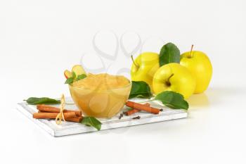 bowl of apple sauce, cinnamon sticks and cloves on wooden cutting board