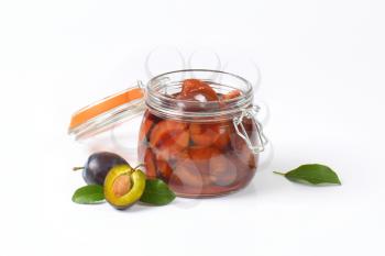 Bottled plums in a glass jar and fresh plums next to it