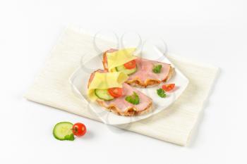 two open faced sandwiches with ham and cheese on white plate and place mat