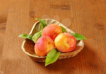 bowl of ripe apricots with leaves on wooden table
