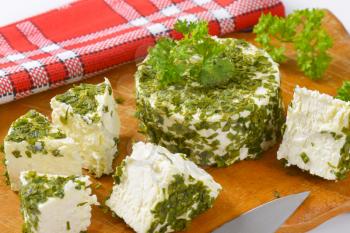 fresh cheese coated in chives and garlic on wooden cutting board