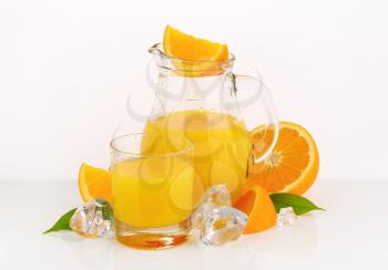 glass and jug of fresh orange juice on white background