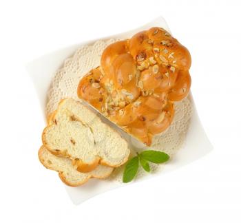 sliced loaf of sweet braided bread with almonds and raisins on white plate