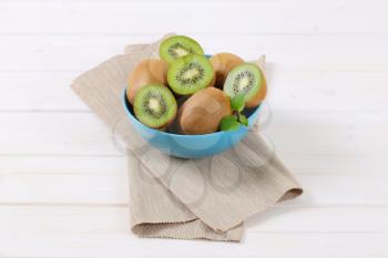 bowl of whole and halved kiwi fruits on beige place mat