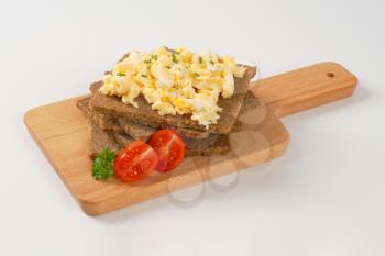 slices of fitness bread with scrambled eggs on wooden cutting board
