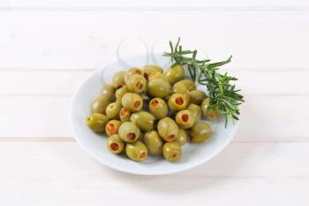 plate of green olives stuffed with red pepper on white background