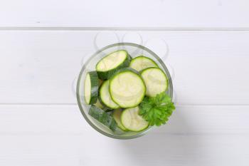 glass of green zucchini slices on white wooden background