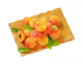 pile of ripe apricots with leaves on wooden cutting board