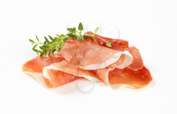 slices of air dried ham with thyme on white background