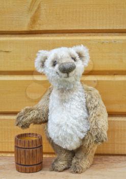 Handmade, the sewed toy: Teddy bear George with a honey keg before a wooden wall