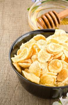 bowl of corn flakes and honey on wooden background