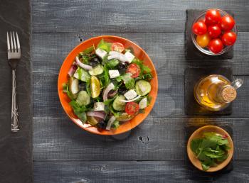 fresh greek salad in plate and ingredients on wooden table