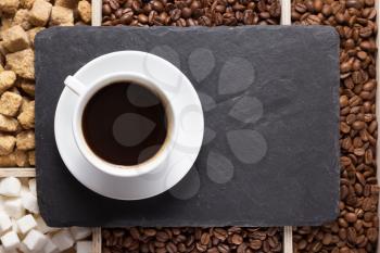 cup of coffee and beans on slate stone black tray background, top view