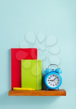 notepad and alarm clock on shelf at wall background surface
